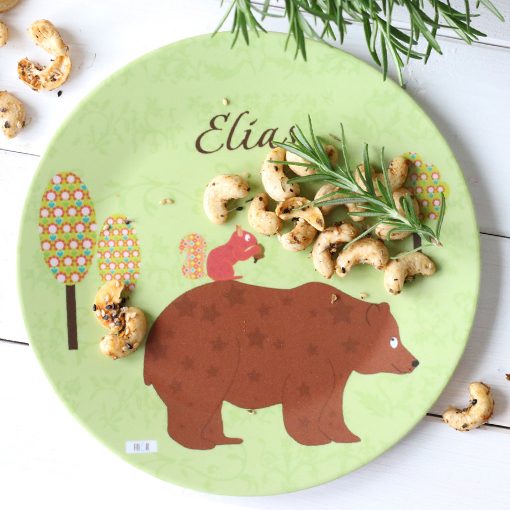 Ein grüner Teller mit einem Bären und einem Eichhörnchen und einem Snack aus Cashewkernen.