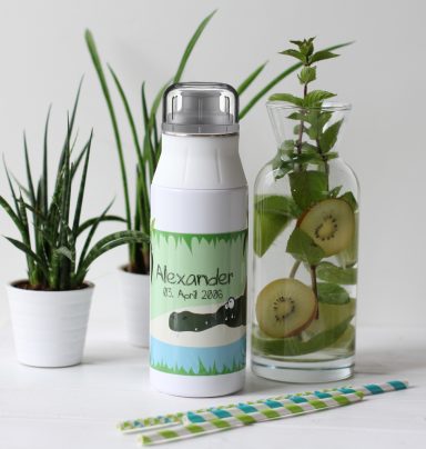 Wasserflasche mit Lavendelmotiv, umgeben von Pflanzen und einer Flasche mit Minze und Apfel.